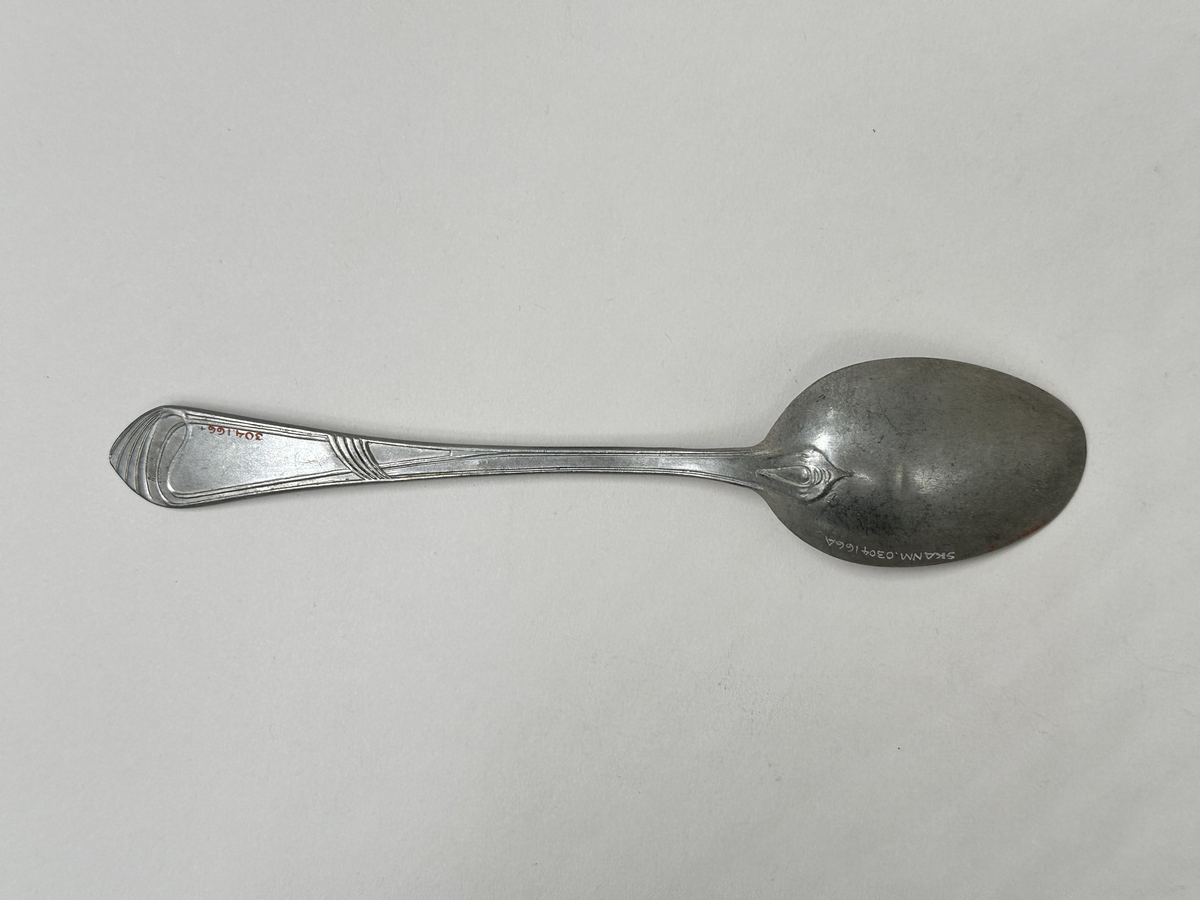 Sked i aluminiumlegering. Dekor av slingor i jugendstil på skaftet. Oregelbunden form på bladet. 