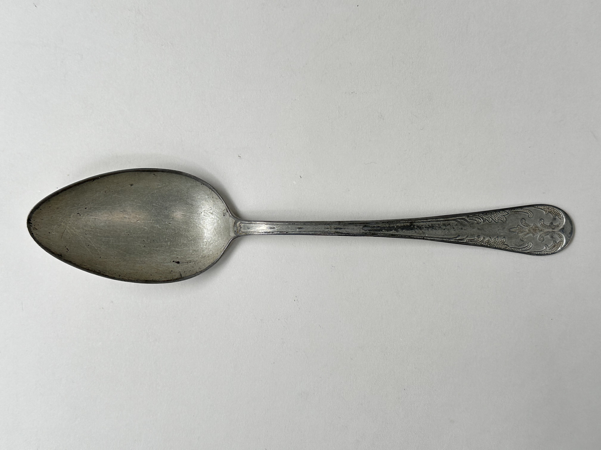 Sked, av vit metallegering. Skaftets ovansida dekorerad med gammalfranskt mönster. Undersidan stämplad med "Alpa Rostskydd Imp."