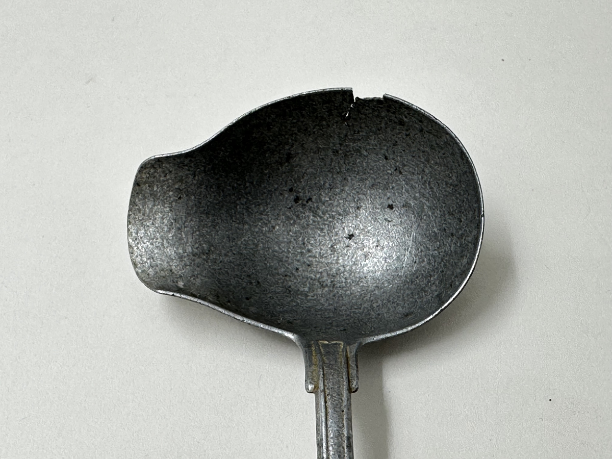 Soppslev i aluminium. Långt skaft, äggformat blad, bred pip. Spricka i bladet upptill. 