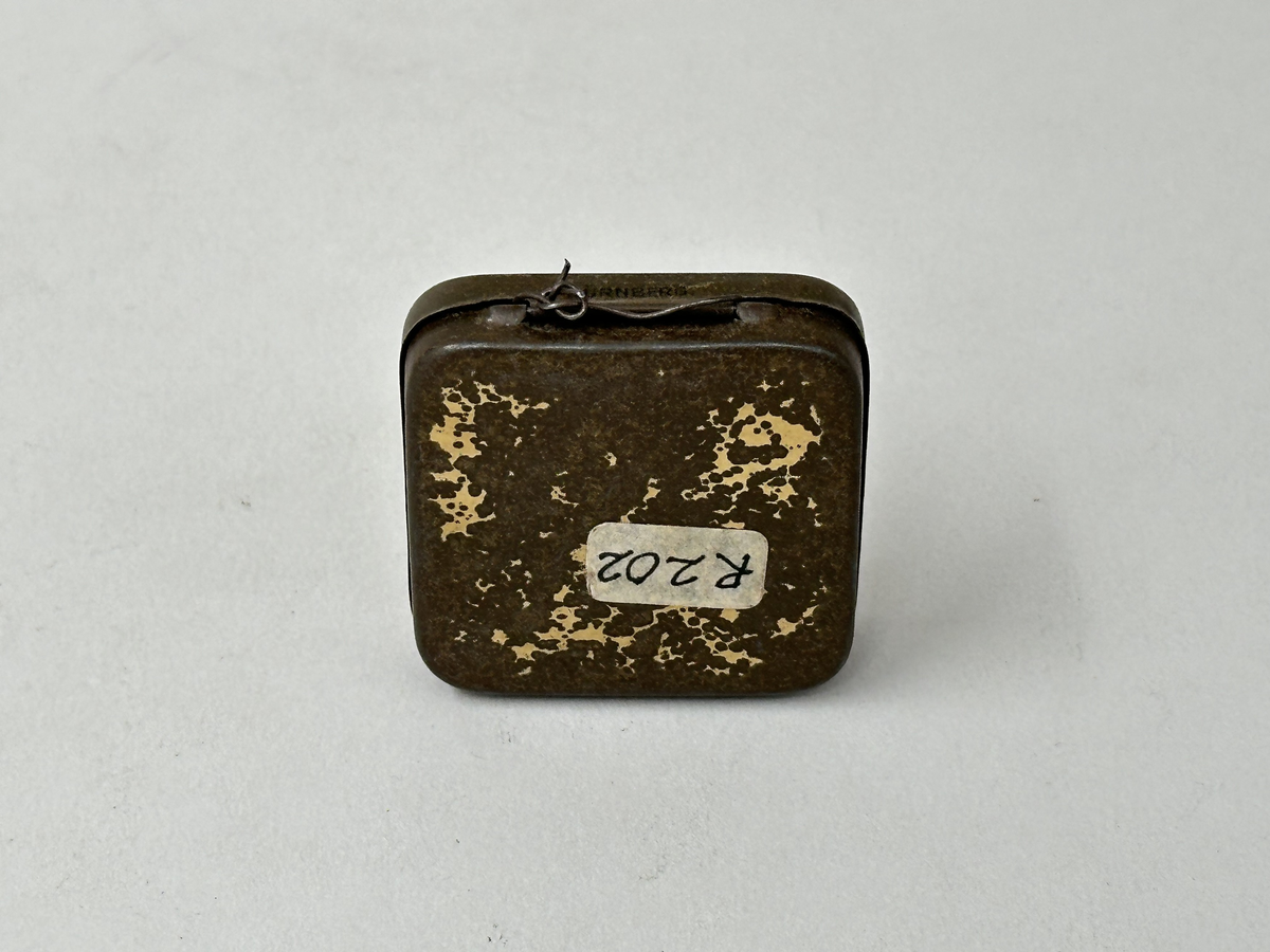 Plåtask med lock. Locket vitt med rund bild: Ryttare med standar mot blå bakgrund, omgiven av bladkrans. Tryckt text: "HOCH-FEINSTE HEROLD-NADELN" "MADE IN GERMANY" "37 D". Innehåller ett skyddspapper och 20 grammofonstift.