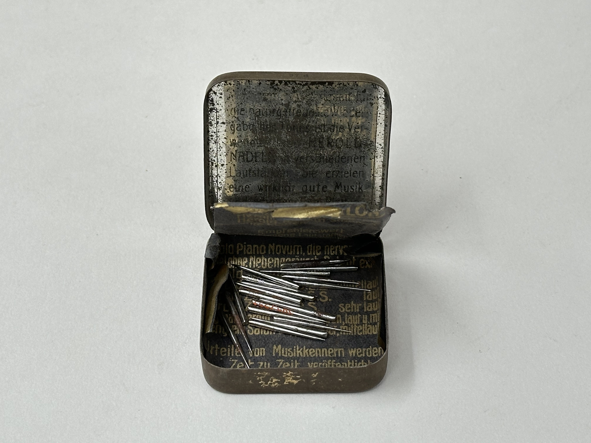 Plåtask med lock. Locket vitt med rund bild: Ryttare med standar mot blå bakgrund, omgiven av bladkrans. Tryckt text: "HOCH-FEINSTE HEROLD-NADELN" "MADE IN GERMANY" "37 D". Innehåller ett skyddspapper och 20 grammofonstift.