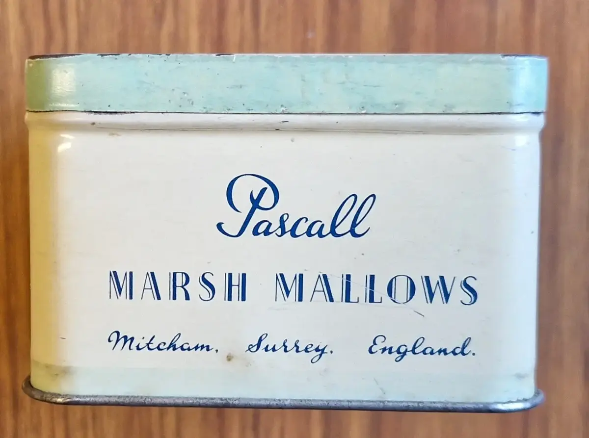 Rektangulär plåtburk i ljusa färger. "Pascall Sunshine. Marsh Mallows" på ovansidan och långsidorna. På kortsidorna "Pascall. Marsh Mallows. Mitcham. Surrey England:".


Anm: Pascalls adress: 100 Blackfriars Road, London, SE1. Också i Mitcham, Surrey.

Den familjeägda firman startades av James Pascall i syfte att tillverka och sälja konfekt.

James Pascall arbetade som agent för Cadbury's innan han startade upp verksamhet med sin bror Alfred i en liten butik på London's Oxford Street 1866.

Till att börja med tillverkade de sötsaker som växtbaserade hostdroppar, godis och hårda franska karameller.

1877 flyttade de till större lokaler i Blackfriars och utvidgade firmans räckvidd.

1897 förstördes deras lokaler i en eldsvåda, startad av en tidigare anställd. Efter eldsvådan flyttade firman till Mitcham, i Surrey.

1922 British Industries Fair Advert for Sweets, Chocolates and Novelties. Also manufacturers of Confectionery and Toys. (Stand No B.8) 
Källa: https://www.gracesguide.co.uk/James_Pascall