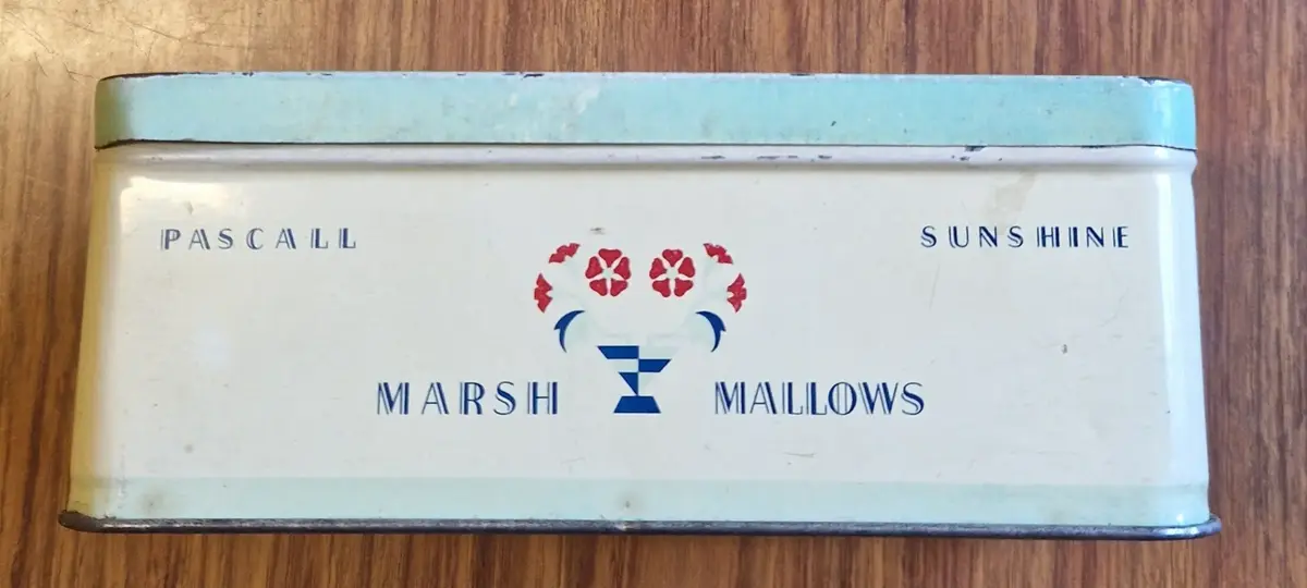 Rektangulär plåtburk i ljusa färger. "Pascall Sunshine. Marsh Mallows" på ovansidan och långsidorna. På kortsidorna "Pascall. Marsh Mallows. Mitcham. Surrey England:".


Anm: Pascalls adress: 100 Blackfriars Road, London, SE1. Också i Mitcham, Surrey.

Den familjeägda firman startades av James Pascall i syfte att tillverka och sälja konfekt.

James Pascall arbetade som agent för Cadbury's innan han startade upp verksamhet med sin bror Alfred i en liten butik på London's Oxford Street 1866.

Till att börja med tillverkade de sötsaker som växtbaserade hostdroppar, godis och hårda franska karameller.

1877 flyttade de till större lokaler i Blackfriars och utvidgade firmans räckvidd.

1897 förstördes deras lokaler i en eldsvåda, startad av en tidigare anställd. Efter eldsvådan flyttade firman till Mitcham, i Surrey.

1922 British Industries Fair Advert for Sweets, Chocolates and Novelties. Also manufacturers of Confectionery and Toys. (Stand No B.8) 
Källa: https://www.gracesguide.co.uk/James_Pascall