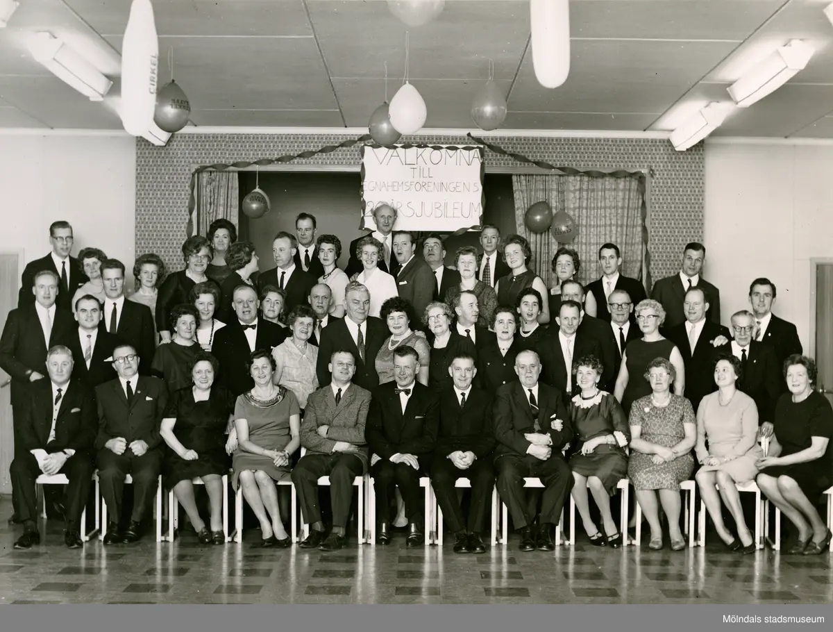 Egnahemsföreningens 20-årsjubileum, okänd plats cirka 1965. Flertalet medlemmar står eller sitter på scenen. Någon håller upp en skylt med texten "VÄLKOMNA TILL EGNAHEMSFÖRENINGENS 20-ÅRSJUBILEUM". Med på bild är (se foto nr två där namnuppgifter framgår): 1. Sten-Allan Johansson, 2. Linnea Andersson, 3. Åke Brorsson, 4. Östen Andersson, 5. Svea Brorsson, 6. Märta Andersson, 7. Artur Andersson, 8. John "Tåa-John" Johansson.