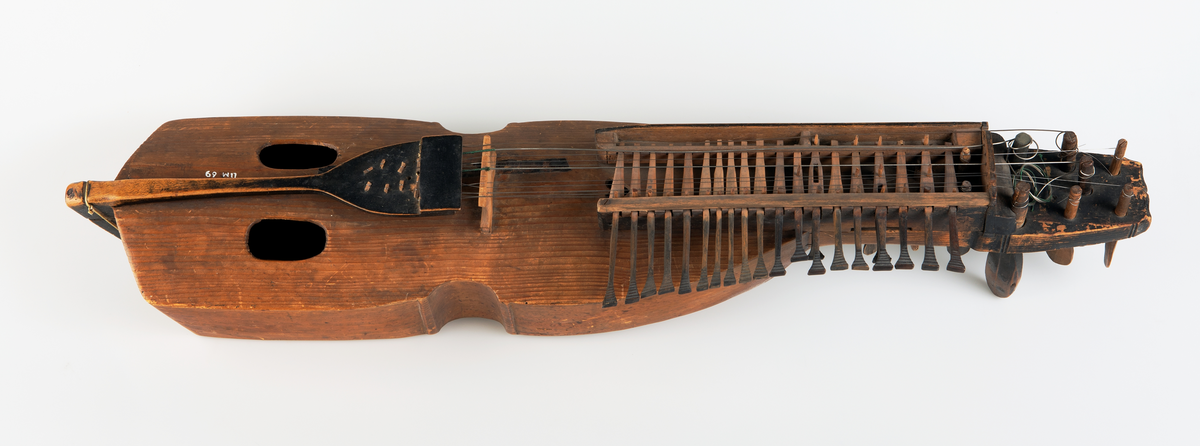 Nyckelharpa, s.k. kontrabasharpa. Korpus bestående av skrov täljt av granträ med lock i granträ. Nyckellåda av lövträ. Nyckellådans överliggare dels intappad dels fastskruvad med järnskruv. Dubbla nyckelrader med i övre raden 19 nycklar och i den undre två. Harpan har tre melodisträngar och ev. bordunsträng. Stränghållare av svartmålat lövträ fastbunden med snöre. Stämskruvar och nycklar av svartmålat lövträ.