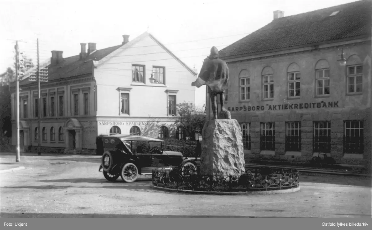 Lilletorget med Glengsgata i Sarpsborg ca. 1920? Statue av Olav den Hellige av kunstneren Gustav  Lærum, avduket 1916. I bakgrunnen bygnignene til Sarpsborg Sparebank og Sarpsborg Aktiekreditbank. Bilen er en 19XX modell, av merke med kjenntegn B ...929.