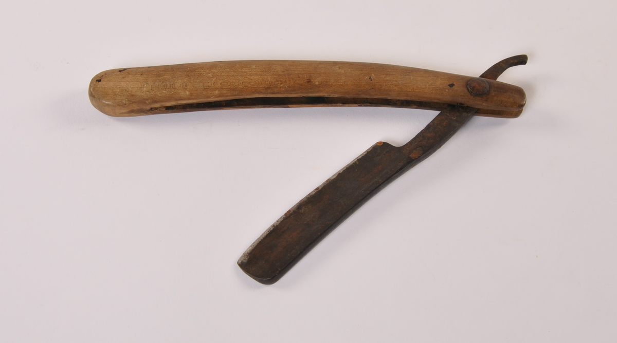 Barberkniv med jernblad til å felle inn i buet treskaft.