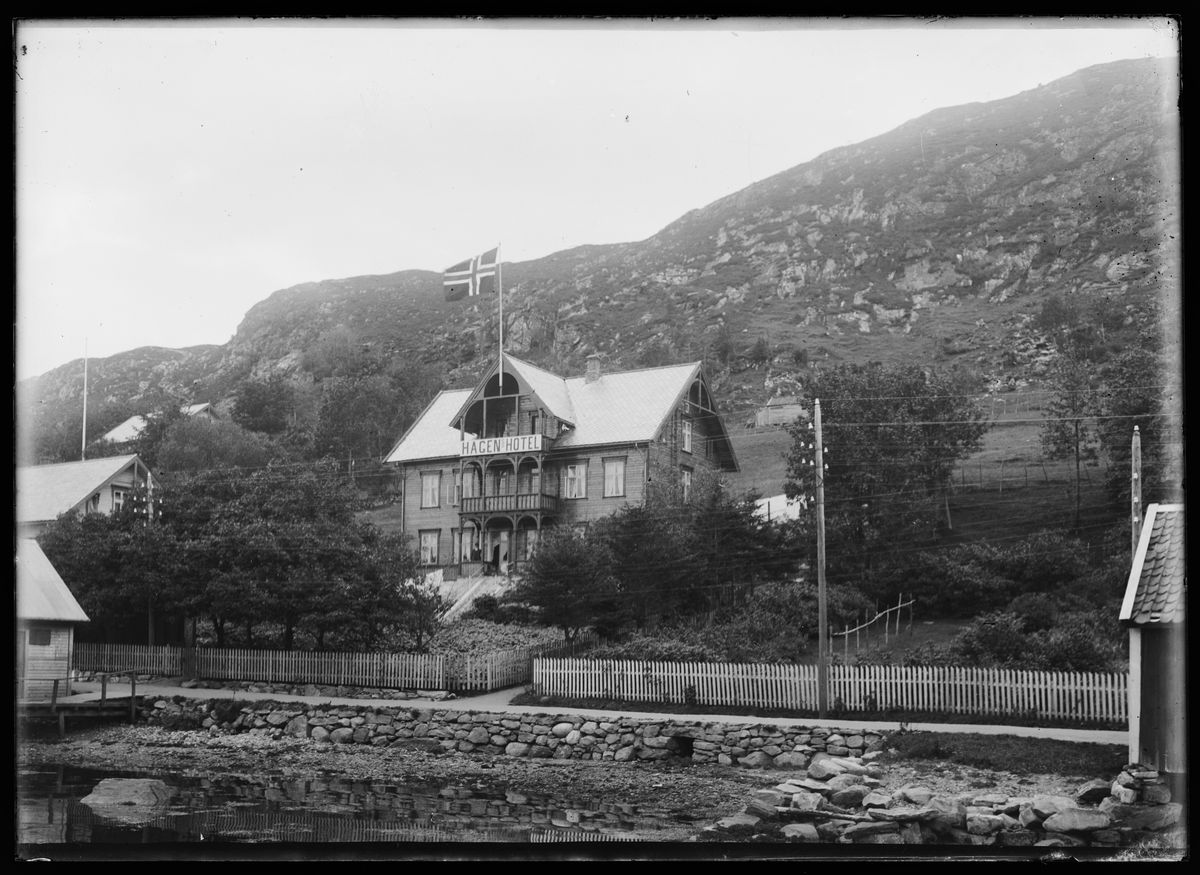 Utsikt til Hagen Hotell. Det er et steingjerde og et tregjerde foran bygningen, og vegetasjon rundt og oppover i åsen i bakgrunnen.