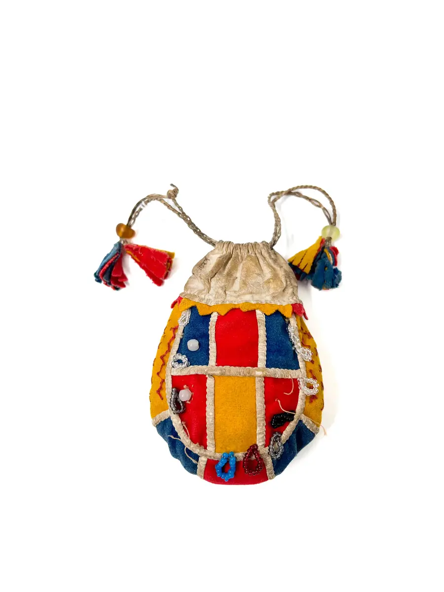  Pung, av kläde och vitt skinn. Handsydd. Överdelen av vitt skinn. Sidorna rundskurna, sydda av bitar av gulrött och klarblått kläde. Bottenstycke av ytterst gult, därefter klarblått och i mitten rött kläde med mellanlägg av dubbelvikt, vitt skinn i sömmarna. Samma typ av mellanlägg i sömmarna mellan sidostyckena och bottenremsan. 

Det ena sidostycket med vita glaspärlor i mitten på varje klädesbit och 15 st öglor gjorda av små glaspärlor, fästade längs kanten på sidostycket. På det andra sidostycket glaspärlor på endast två klädesbitar och 10 st öglor av pärltråd längs kanten. 

Överdel av vitt skinn, sydd av dubbelt skinn med dragsko upptill, dragskon öppen åt båda sidor, genom dragskon två snören, tvinnade av smala skinnremmar med tofsar av klarblått, rött och gult kläde. 

Dragsnörena hålls ihop parvis av en glaspärla, varigenom de är trädda. Sömmarna sydda med bomullstråd och något slags vaxad tråd.