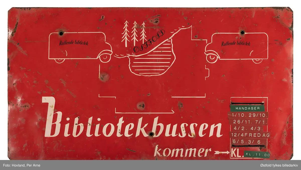 Skiltet har tegning i hvitt på rød bunn, viser bokbussen og vann og trær. Rullende bibliotek.