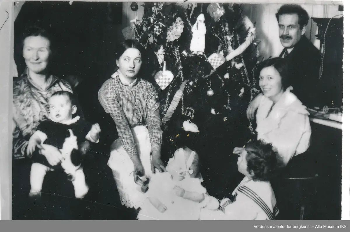 Nordlysobservatoriet på Haldde, juletre, piano, 4 voksne, 3 barn, jula 1916.
Julefeiring på Haldde 1916 rundt juletre. Kledd i kjole og hvitt. Alle ser ut til å være distrahert av noe og kun Ole Andreas Krogness Senior ser på kamera.