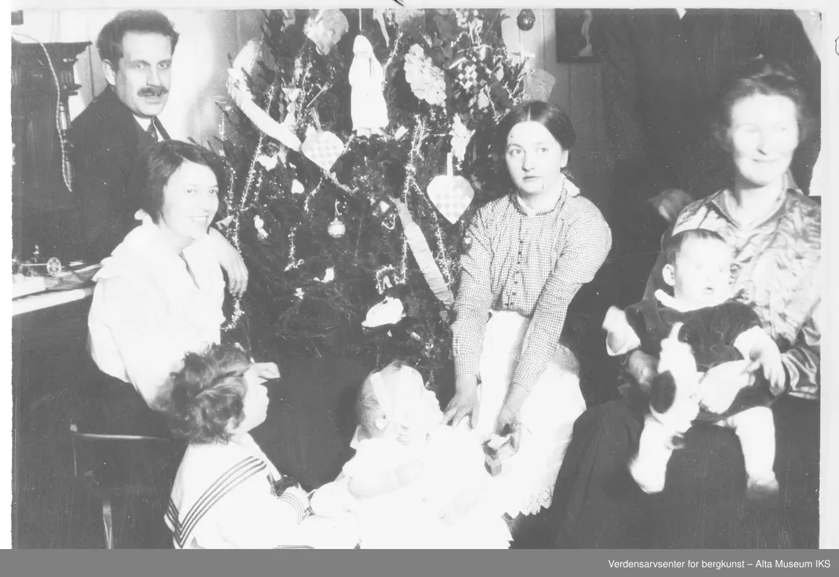 Nordlysobservatoriet på Haldde, juletre, piano, 4 voksne, 3 barn, jula 1916.
Julefeiring på Haldde 1916 rundt juletre. Kledd i kjole og hvitt. Alle ser ut til å være distrahert av noe og kun Ole Andreas Krogness Senior ser på kamera.