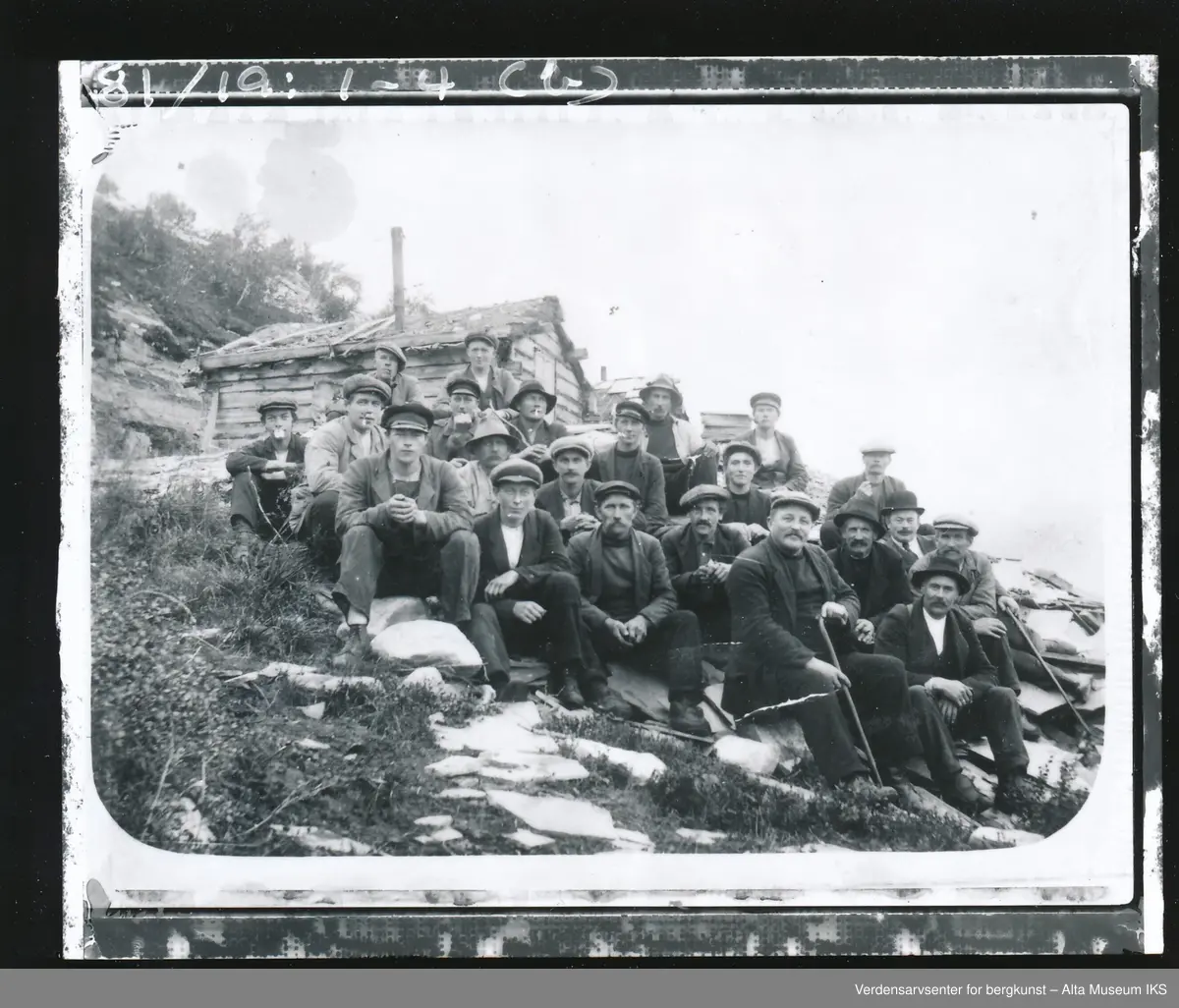 Gruppebilde av skiferarbeidere, Storhalla, Pæska, Alta Kommune.
John R. Heitmans skiferstue i bakgrunnen. Ole Borkhus sin skiferstue i forgrunnen.
Navneliste skal finnes.