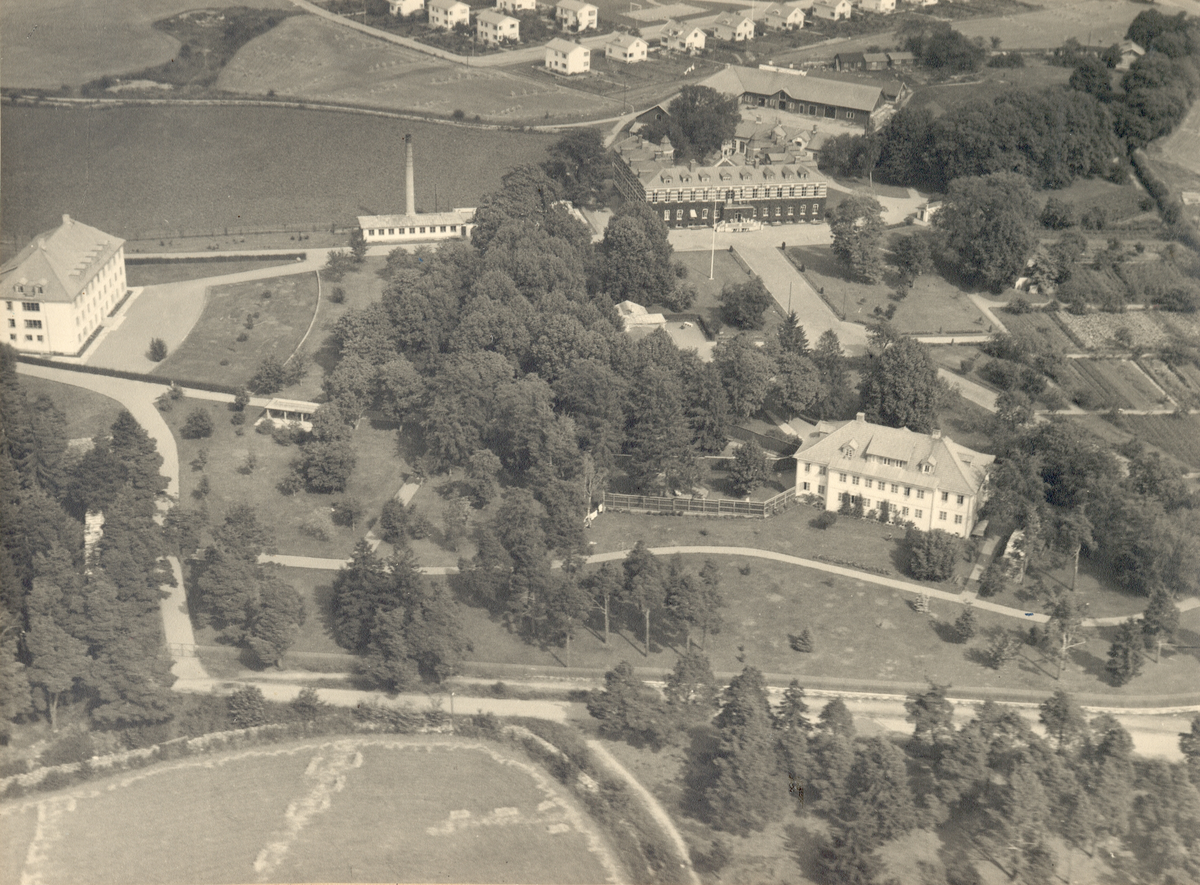 Flygfoto över Kalmar ålderdomshem med två tillhörande sjukhus. En ladugård ligger precis bakom det ena sjukhuset.
