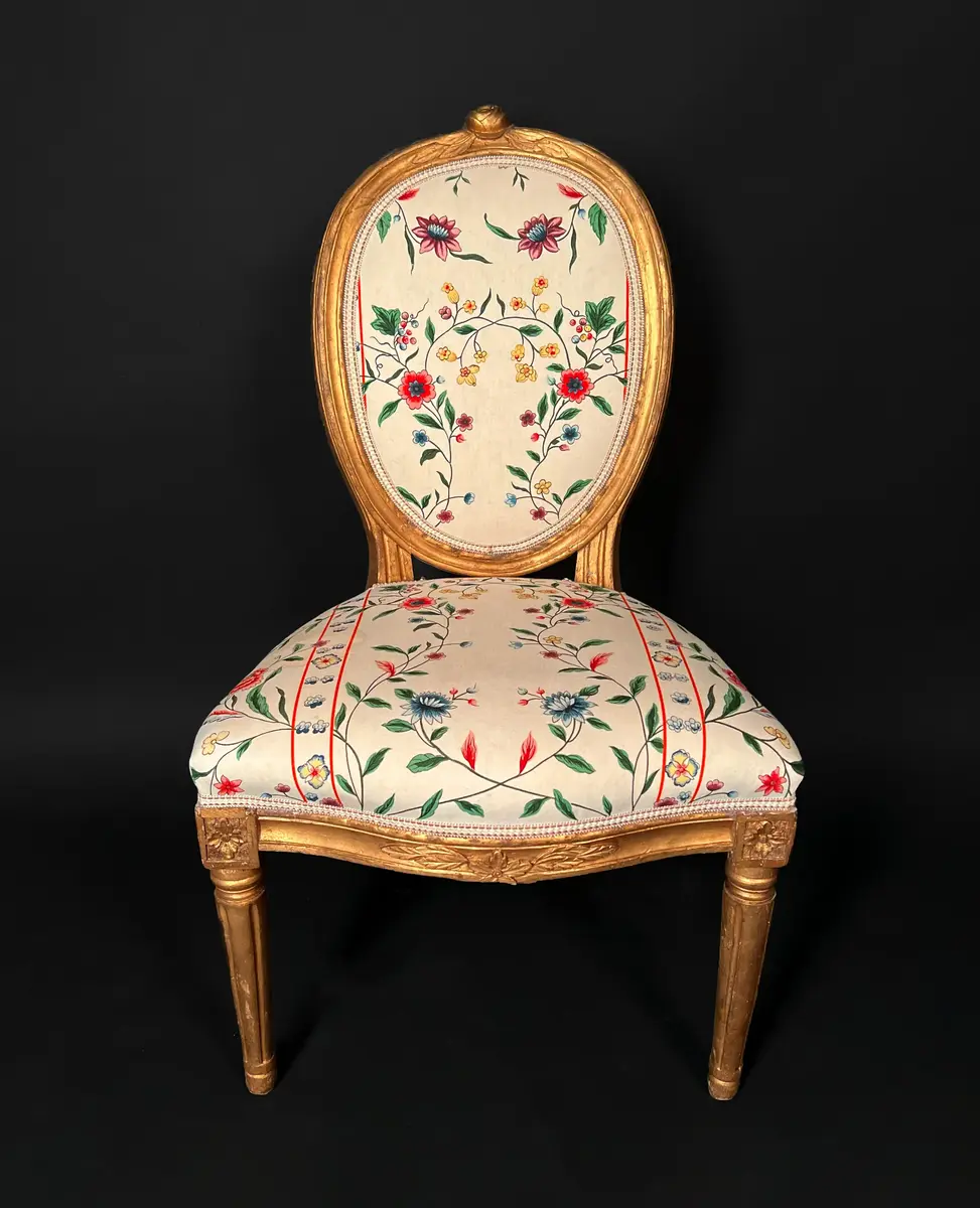 Ett par stolar i gustaviansk stil. Raka, räfflade och neråt avsmalnande ben. Sargen är rak och prydd med hörnrosetter ovanför benen. Framsargen har en blomdekor i mitten. Ryggen har en oval form och är krönt med en snidad ros. Ryggens mitt samt stolens sits är stoppade och klädda i ett vitt tyg med blomsterdekor i grönt, rött och blått. Stolens stomme är förgylld. Ursprungligen har stolen varit klädd i svart läder och ryggens baksida med rött tyg.