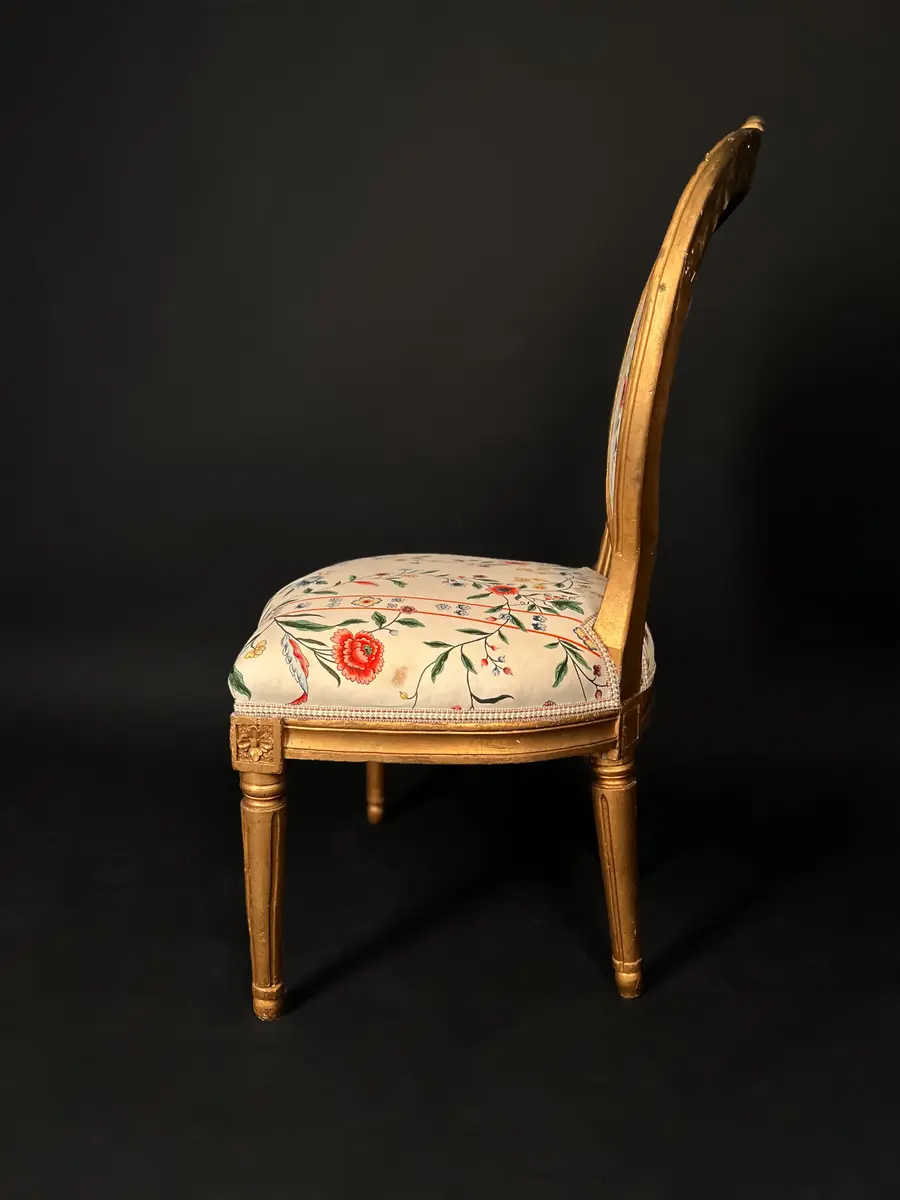 Ett par stolar i gustaviansk stil. Raka, räfflade och neråt avsmalnande ben. Sargen är rak och prydd med hörnrosetter ovanför benen. Framsargen har en blomdekor i mitten. Ryggen har en oval form och är krönt med en snidad ros. Ryggens mitt samt stolens sits är stoppade och klädda i ett vitt tyg med blomsterdekor i grönt, rött och blått. Stolens stomme är förgylld. Ursprungligen har stolen varit klädd i svart läder och ryggens baksida med rött tyg.