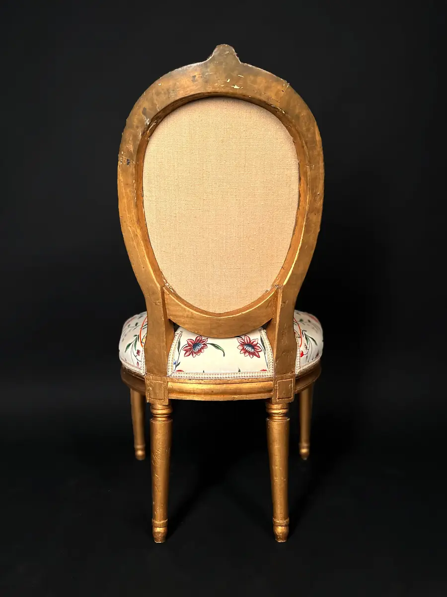 Ett par stolar i gustaviansk stil. Raka, räfflade och neråt avsmalnande ben. Sargen är rak och prydd med hörnrosetter ovanför benen. Framsargen har en blomdekor i mitten. Ryggen har en oval form och är krönt med en snidad ros. Ryggens mitt samt stolens sits är stoppade och klädda i ett vitt tyg med blomsterdekor i grönt, rött och blått. Stolens stomme är förgylld. Ursprungligen har stolen varit klädd i svart läder och ryggens baksida med rött tyg.