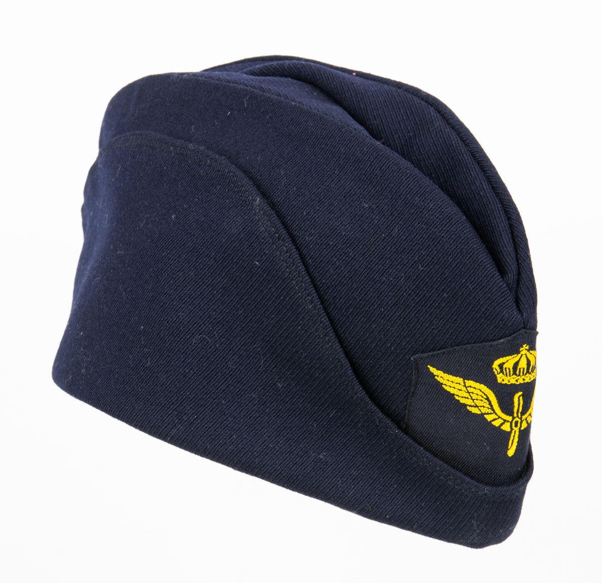 Blå flygmössa med flygemblem m/51. FLygemblemet är 70 mm och sitter mitt fram. På höger insida är det i rött stämplat de tre kronorna samt "57 Ö. S. B"