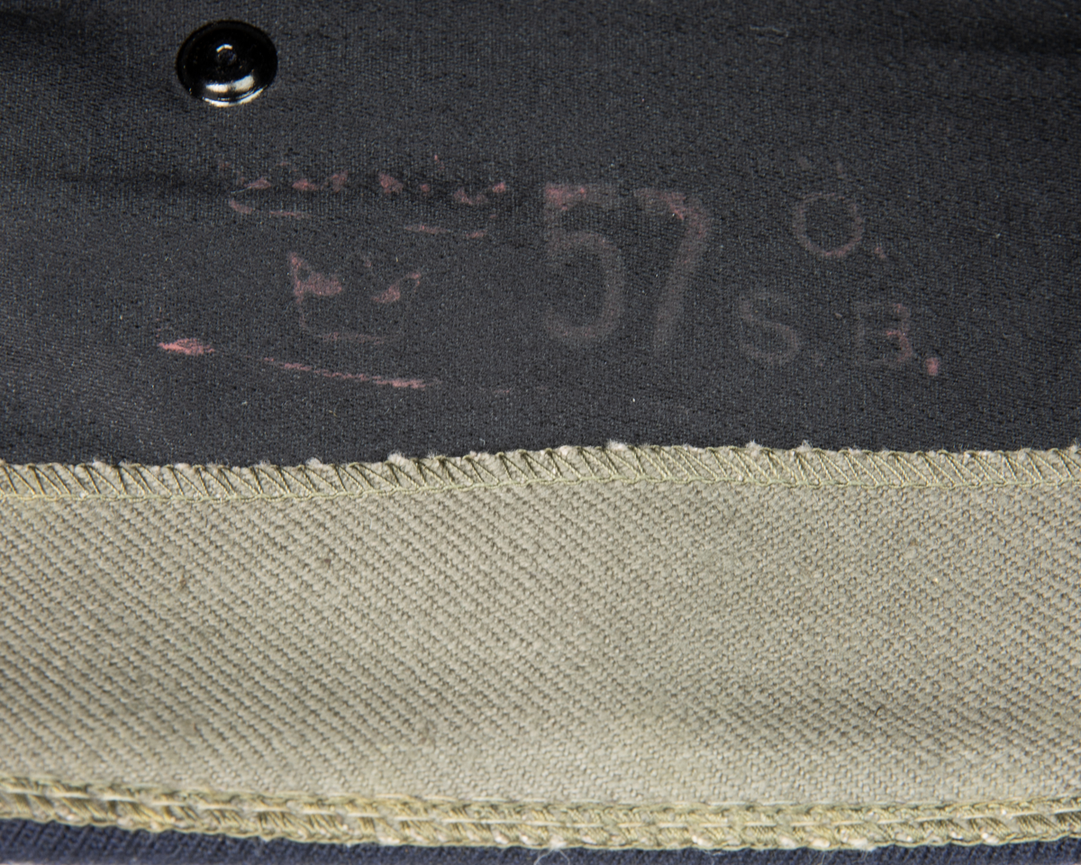 Blå flygmössa med flygemblem m/51. FLygemblemet är 70 mm och sitter mitt fram. På höger insida är det i rött stämplat de tre kronorna samt "57 Ö. S. B"