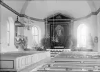 Interiör av Vårdnäs kyrka 1903. Vid fototillfället lövad för konfirmation eller annan högtidlighet. Altartavlan färdigställdes av Pehr Hörberg 1802, ett fåtal år efter kyrkans invigning.