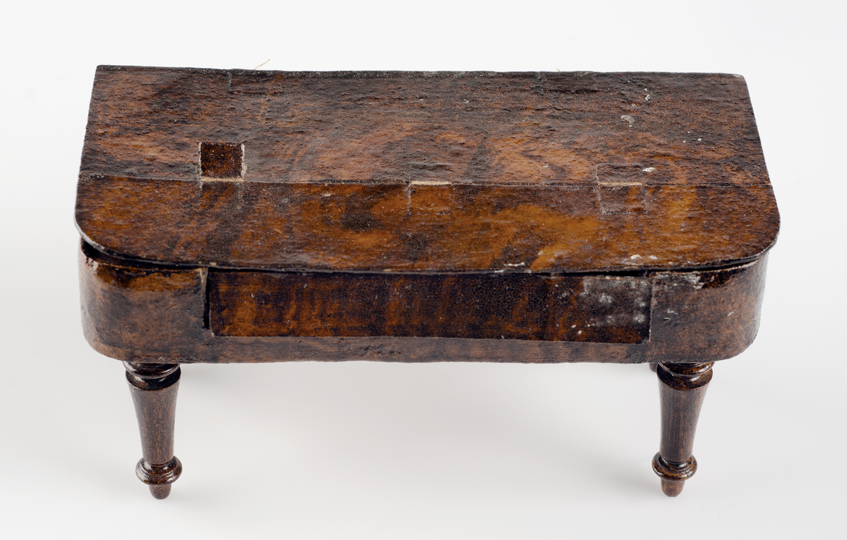 Leksak, taffel av mörkbrun och gulflammig ädelträimitation. Klaviatur av papper. På undersidan står med bläck: i Rde 20 öre. 