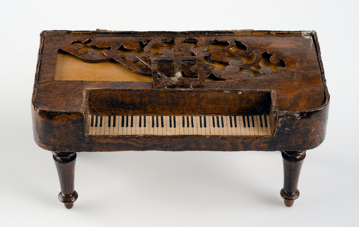 Leksak, taffel av mörkbrun och gulflammig ädelträimitation. Klaviatur av papper. På undersidan står med bläck: i Rde 20 öre. 