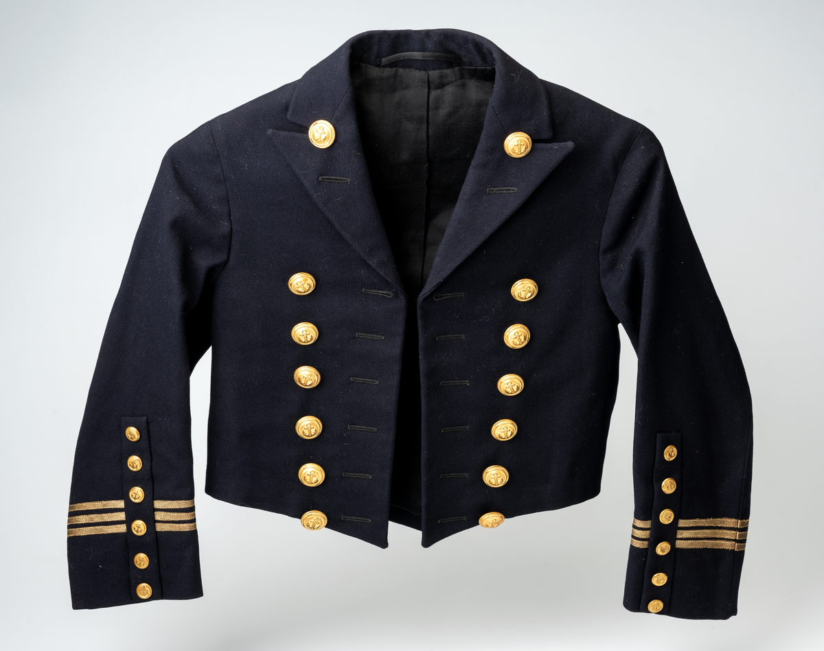 Matrossdress jakke og vest: Dobbelspent, mørkeblå matrosjakke i ull m. seks gullknapper og seks knappehull i hver side. En knapp og et knappehull på hvert jakkeslag. Distinksjoner på ermene:  tre striper med påsydde smale gullbånd. Seks mindre knapper nederst på ermene. Skråsydd ned midt foran og midt bak. Kort modell. Sort forstoff innvendig, hvit forstoff i ermene. Hempe i nakken, liten innerlomme i høyre side m. maskinsydd monogram. Anker på knappene.
Mørkeblå matrosvest i ull m. seks gullknapper i front og to lommer i hver side. Bakstykke i sort blankt stoff m. belte og spenne, liten splitt MB. Hvitt forstoff invendig.