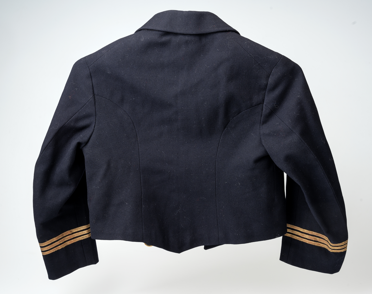 Matrossdress jakke og vest: Dobbelspent, mørkeblå matrosjakke i ull m. seks gullknapper og seks knappehull i hver side. En knapp og et knappehull på hvert jakkeslag. Distinksjoner på ermene:  tre striper med påsydde smale gullbånd. Seks mindre knapper nederst på ermene. Skråsydd ned midt foran og midt bak. Kort modell. Sort forstoff innvendig, hvit forstoff i ermene. Hempe i nakken, liten innerlomme i høyre side m. maskinsydd monogram. Anker på knappene.
Mørkeblå matrosvest i ull m. seks gullknapper i front og to lommer i hver side. Bakstykke i sort blankt stoff m. belte og spenne, liten splitt MB. Hvitt forstoff invendig.