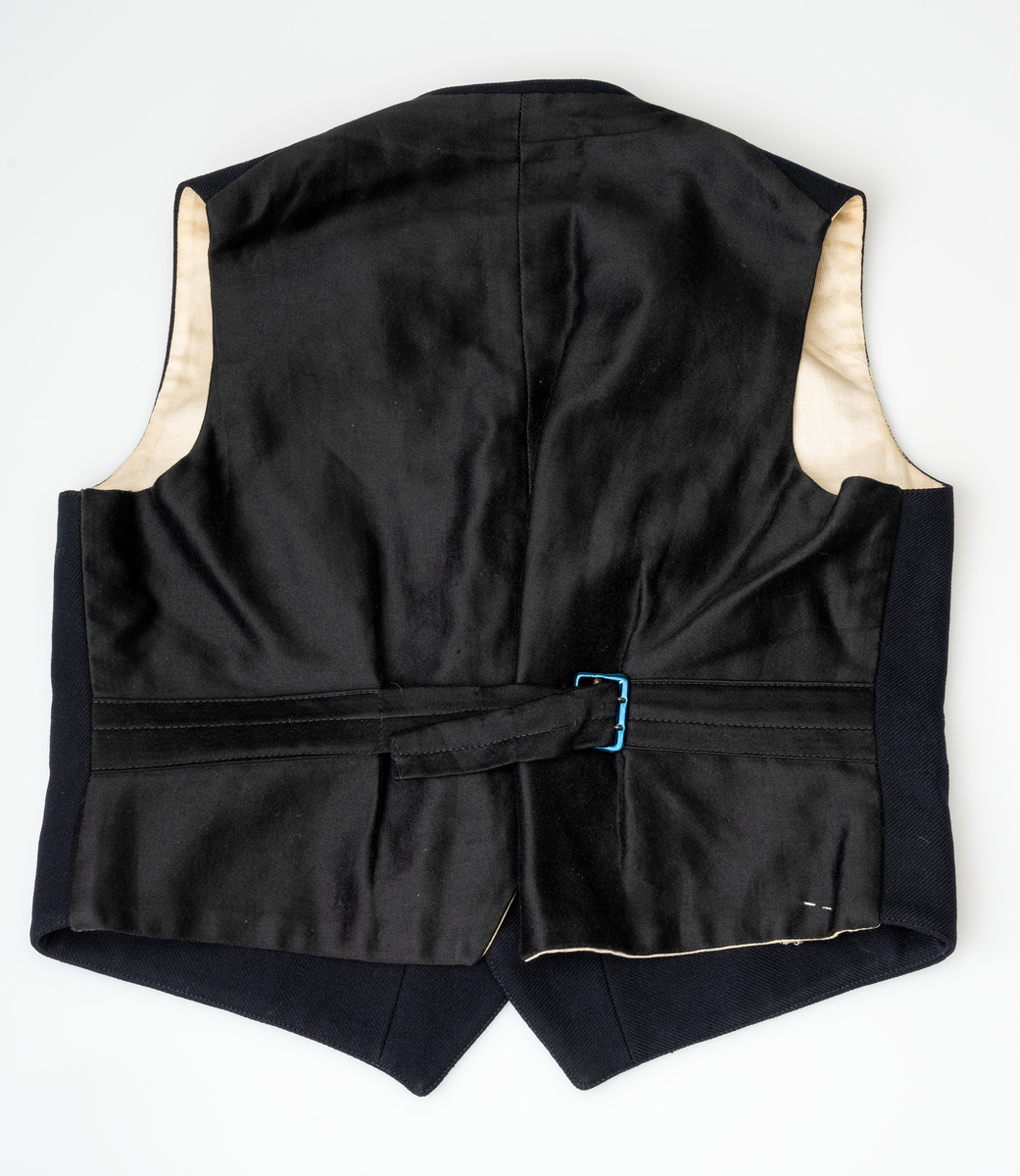 Matrossdress jakke og vest: Dobbelspent, mørkeblå matrosjakke i ull m. seks gullknapper og seks knappehull i hver side. En knapp og et knappehull på hvert jakkeslag. Distinksjoner på ermene:  tre striper med påsydde smale gullbånd. Seks mindre knapper nederst på ermene. Skråsydd ned midt foran og midt bak. Kort modell. Sort forstoff innvendig, hvit forstoff i ermene. Hempe i nakken, liten innerlomme i høyre side m. maskinsydd monogram. Anker på knappene.
Mørkeblå matrosvest i ull m. seks gullknapper i front og to lommer i hver side. Bakstykke i sort blankt stoff m. belte og spenne, liten splitt MB. Hvitt forstoff invendig.