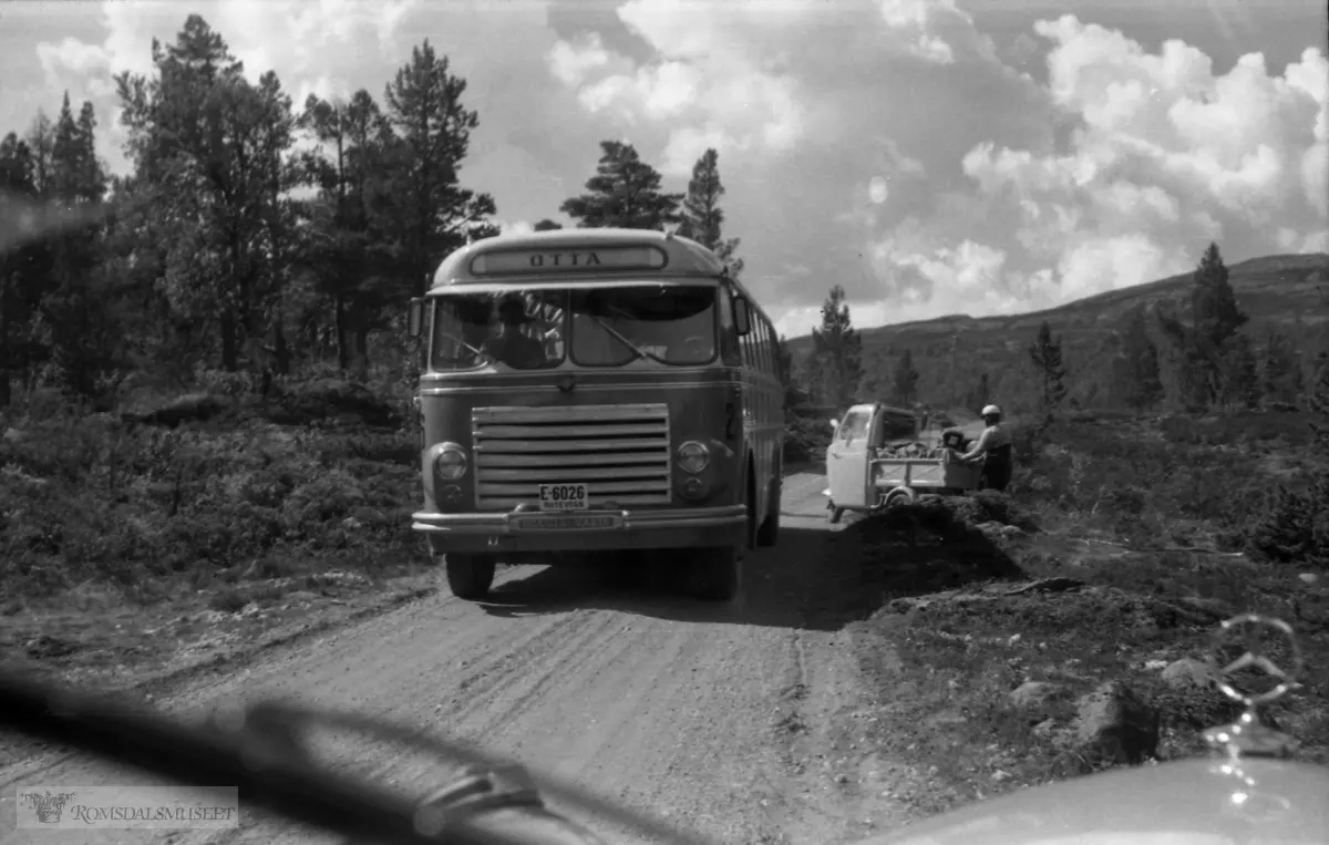 "Ferietur 1959"."Geiranger - Valdres".E-6026 er en Scania-Vabis 1955 med karosseri fra Brødrene Knudsen, tilh. Ottadalen Kommunale Billag. Kilde: Bussbasen til Rutebilhistorisk Forening. Til høyre en Piaggio Vespa Ape (arbeidsbie på itailensk), en scooterbasert laste-/varebil som aldri slo helt gjennom i Norge.