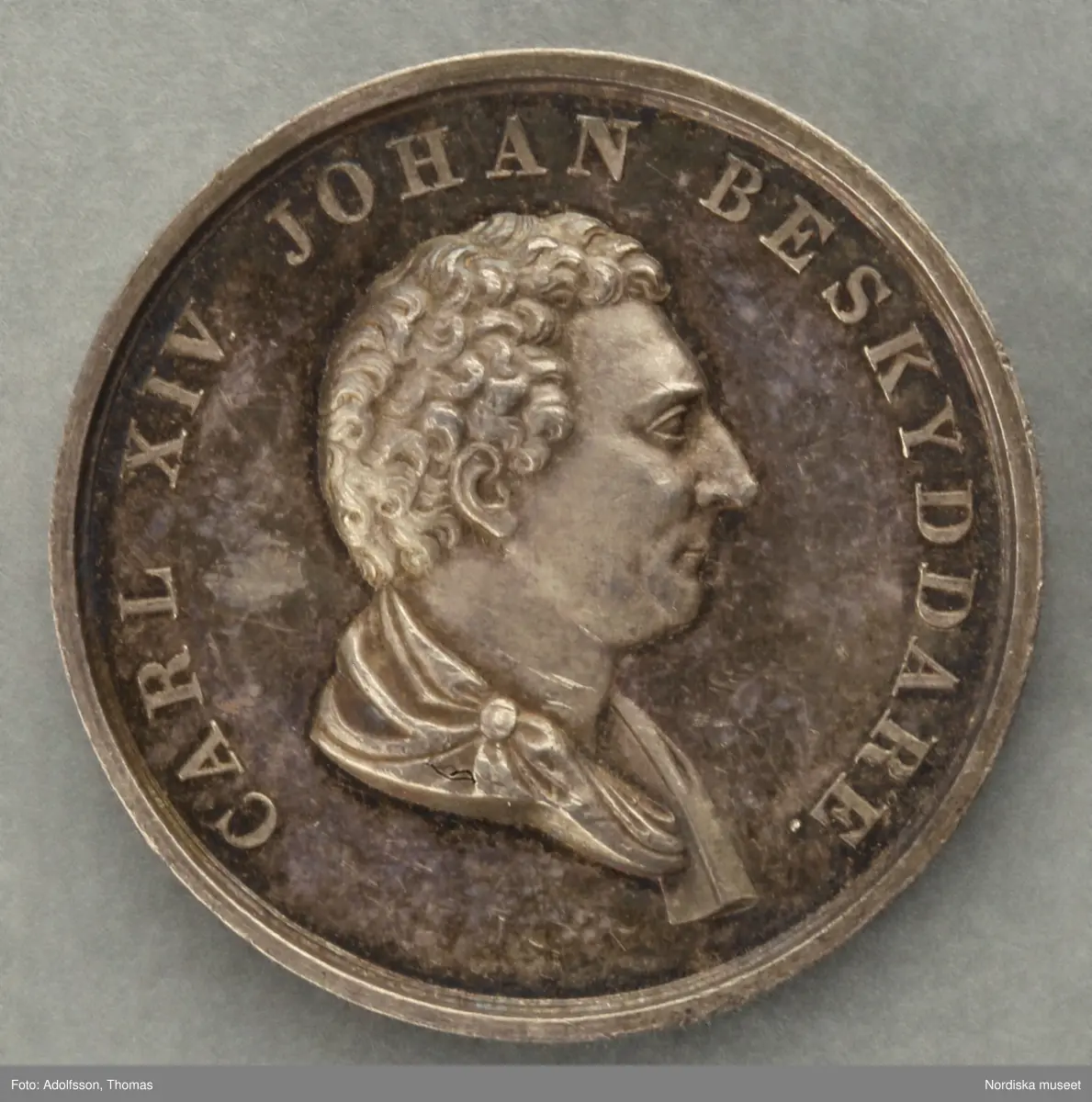 Huvudliggaren:
a-c
"3 minnespenningar. Öfver Karl XIV Johan.
a) I silfver. Jmfr Hildebrand, del II, sid 344, nr 34
b) I silfver. Jmfr H-d. del II, sid 345, nr 35.
c) I brons. Lika med b.