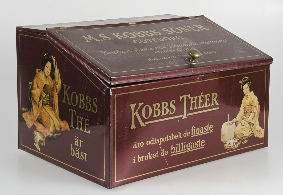 Mörkröd med text i guld "M. S. Kobbs söner Göteborg, Nordens äldsta och förnämsta theimport. Etablerad 1809, kontrollant Doktor J. E. Alén". På fram- och baksida "Kobbs theér äro odiskutabelt de finaste i bruket de billigaste". På kortsidorna "kobbs thé är bäst". Polykrom dekor. Lockets insida har en påklistrad ljusbrun pappersetikett med brun text med råd om förvaring av té.
 
