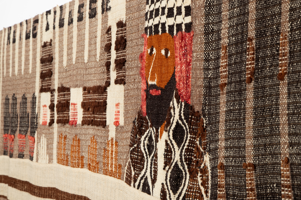 Todelt motiv, med figurativ frise øverst og nonfigurative/asbstrakte fargefelt med arkitektoniske elementer i nedre del. Motivet i øvre del av verket er delt inn som et figurativt triptyk. I heraldisk høyre panel ser vi en representasjon av en ikke navngitt etiopisk kvinne, og ved siden av henne følger ornamenter som også kan leses figurativt som spyd eller piggtråd. I midtpanelet sees en mannsfigur med hatt. Han betegnes noen steder som Storbritannias utenriksminister Anthony Eden, andre ganger som den franske politikeren Pierre Laval, den italienske kongen Vittorio Emanuele III eller Italias ambassadør i Etiopia. Deretter følger ni hender som rekkes opp som i forsvar fra frisens nedre linje. I den andre enden av midtfeltet er Etiopias keiser Haile Selassie fremstilt; hans navn er også vevd inn med bokstaver øverst i feltet, over hendene. I heraldisk venstre panel ser vi en representasjon av en anonym etiopier med Benito Mussolinis avhugde hode på et spyd. Under hodet sees bokstavene "hr. M", vevd i rødt.
