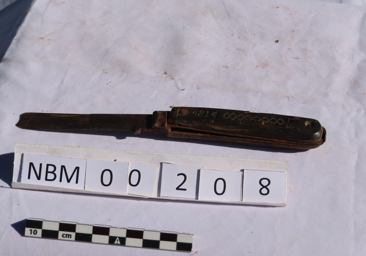 Skaft av tre på ene siden, av horn (?), sort på andre siden.
På hornsiden skåret 1834 og E, og svidd bord.