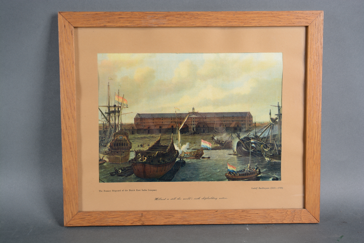 Rektangulært, polykromt trykk med motiv som viser et gammelt, hollandsk skipsverft med en lang bygning i bakgrunnen og flere skip med nederlandske flagg på vannet i forgrunnen. Trykket er omkranset av passepartout i beige kartong, det er rammet inn i en enkel treramme og med beskyttende glass.