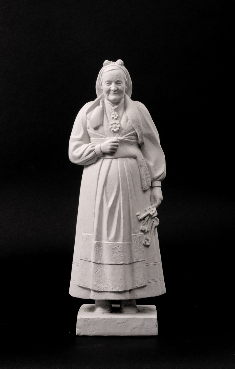 Kvinne iført folkedrakt, heilfigur, med eit knippe nyklar.
