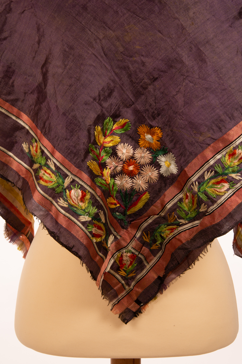 Firkantet sjal av silke, med lilla bunnfarge og striper som border rundt ved kanten i to ulike utforminger. I det ene hjørnet er det brodert på blomster som dekor.