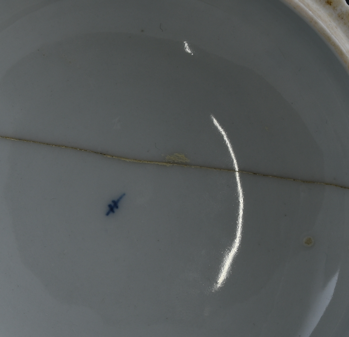 Sukkerskål av glassert porselen, med lokk. Skålen har hvit grunnfarge, og håndmalt dekor av blått stråmønster, eller musselmaling. Skålen og lokket er kannelert på utsiden. En knott på lokket har form nesten som spisskål. Lokket har knekt i to og bollen har avknekt et skår, begge er limt sammen igjen.