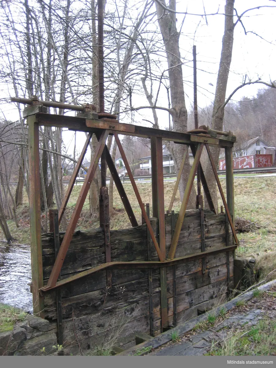 Närbild på en dammlucka över Mölndalsfallen söderut med omgivande träd, Mölndal år 2011. I fonden till höger skymtas Pixbovägen och villor på Sågdalsgatan. Dokumentation inför ombyggnation.
Relaterade motiv: 2024_1365 - 1412.