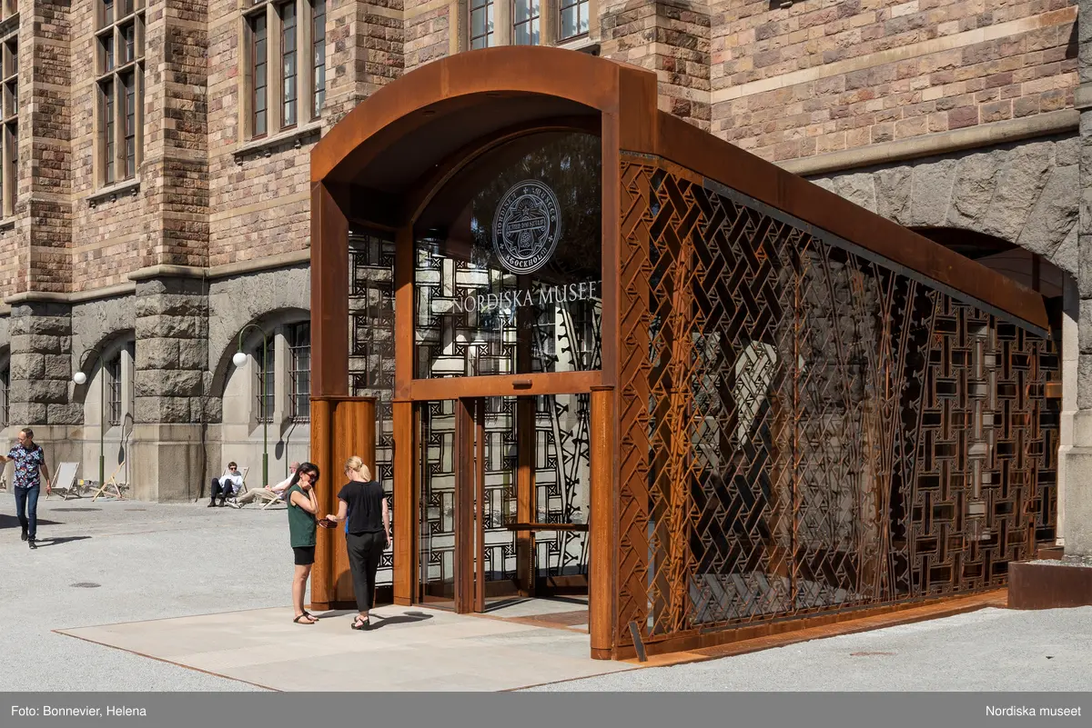 Exteriörer från Nordiska museets västra sida, bakgården, med den nya entrén och byggnaden Lusknäppen. Entrén är ritad av Lone-Pia Bach. Konstnären Outi Pieski står för den konstnärliga gestaltningen med konstverket Two Directions, inspirerat av föremål ur museets samiska samlingar.