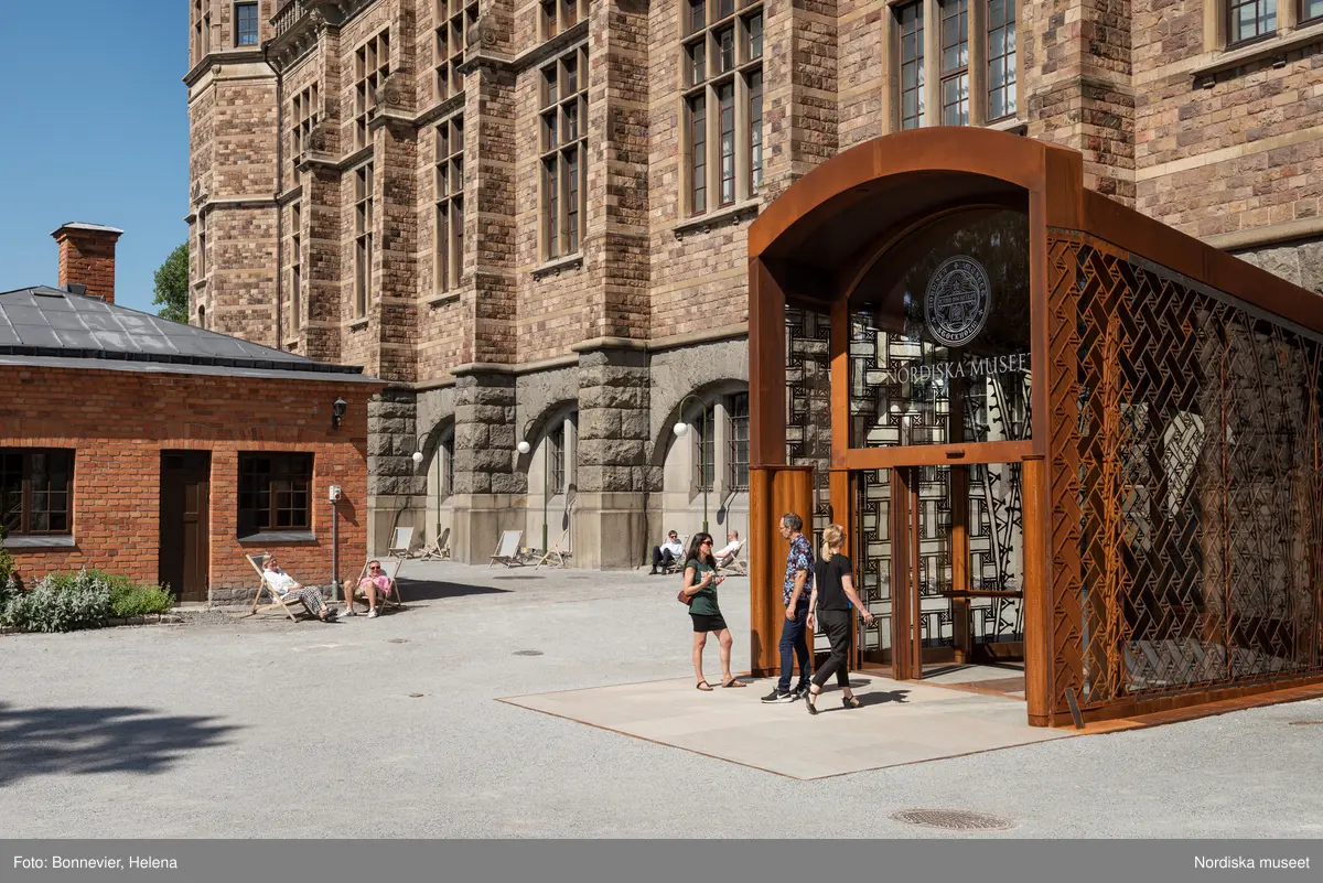 Exteriörer från Nordiska museets västra sida, bakgården, med den nya entrén och byggnaden Lusknäppen. Entrén är ritad av Lone-Pia Bach. Konstnären Outi Pieski står för den konstnärliga gestaltningen med konstverket Two Directions, inspirerat av föremål ur museets samiska samlingar.