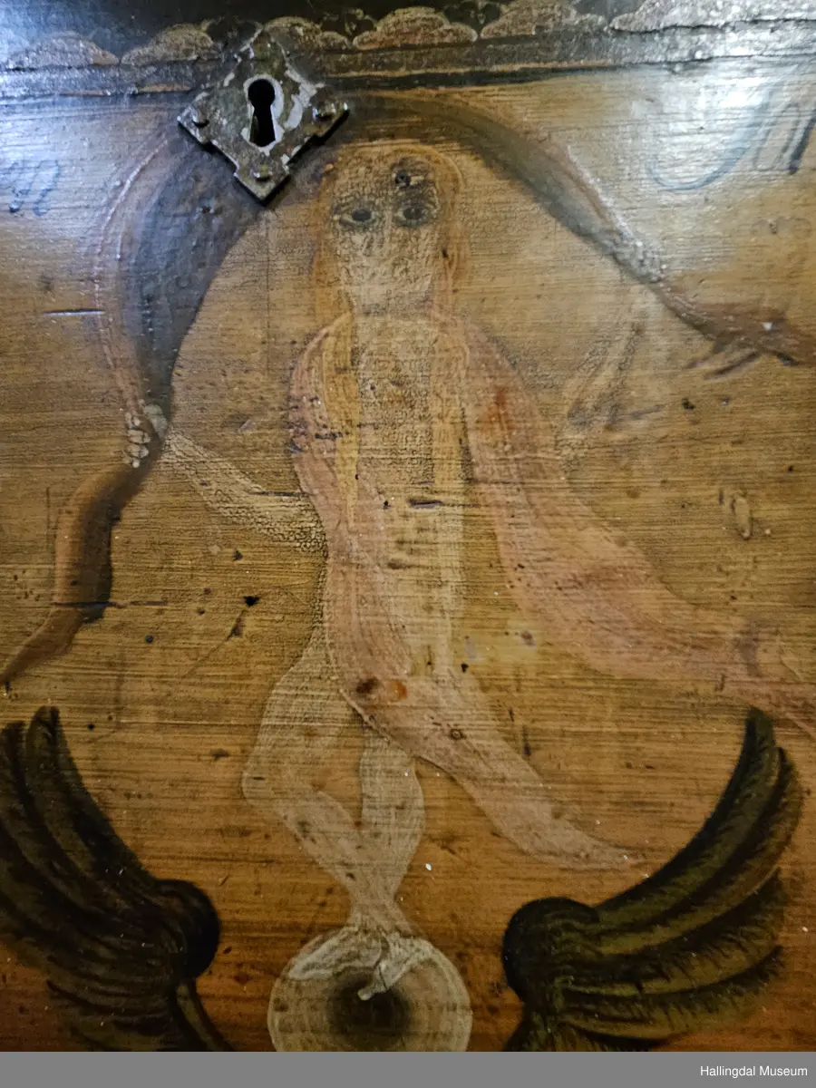Skatoll med 3 like store skuffer pluss en mindre skuff over disse. På sidene av den øverste skuffen er det støtter som kan dras ut til platen som kan legges ned.  Platen er malt med 3 ulike motiv: Til venstre Maria og Josef med Jesusbarnet og 2 esler i stallen. I midten: En engel med rosa sjal som holder over hodet et brunt klede. Engelen står oppå en kule over englevinger. Til høyre: Jesus på korset med 2 damer og 2 menn.  
De 3 nederste skuffene er malt, 4 rosebuketter på hver skuff. Understellet er utskjært, ranke. 
Bak platen er det 6 små skuffer på hver side av et åpent rom.  Oppå skuffene og platen er det et buet skap med 2 hyller og øverst hylle for tallerker eller skjeer. Dørene har utskjærte speil som er rosemalt. Dørene er gråmalt på baksiden.
Bunnfargen på skatollet er mørk grønt og noe er brunrødt.
