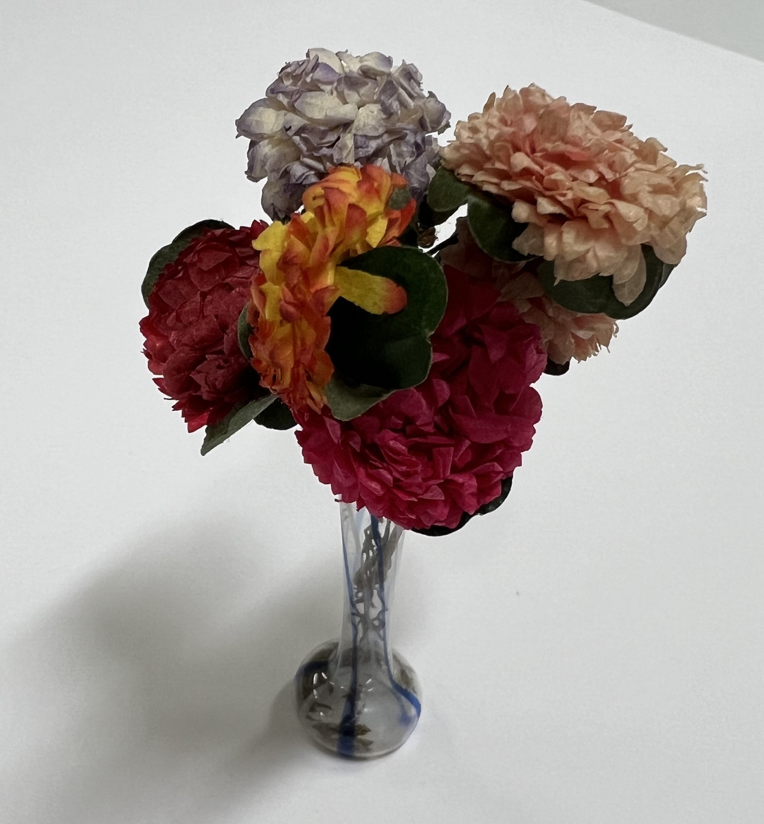 Glasvas med blå ränder. Pappersblommor i rosa, lila, gult och grönt.