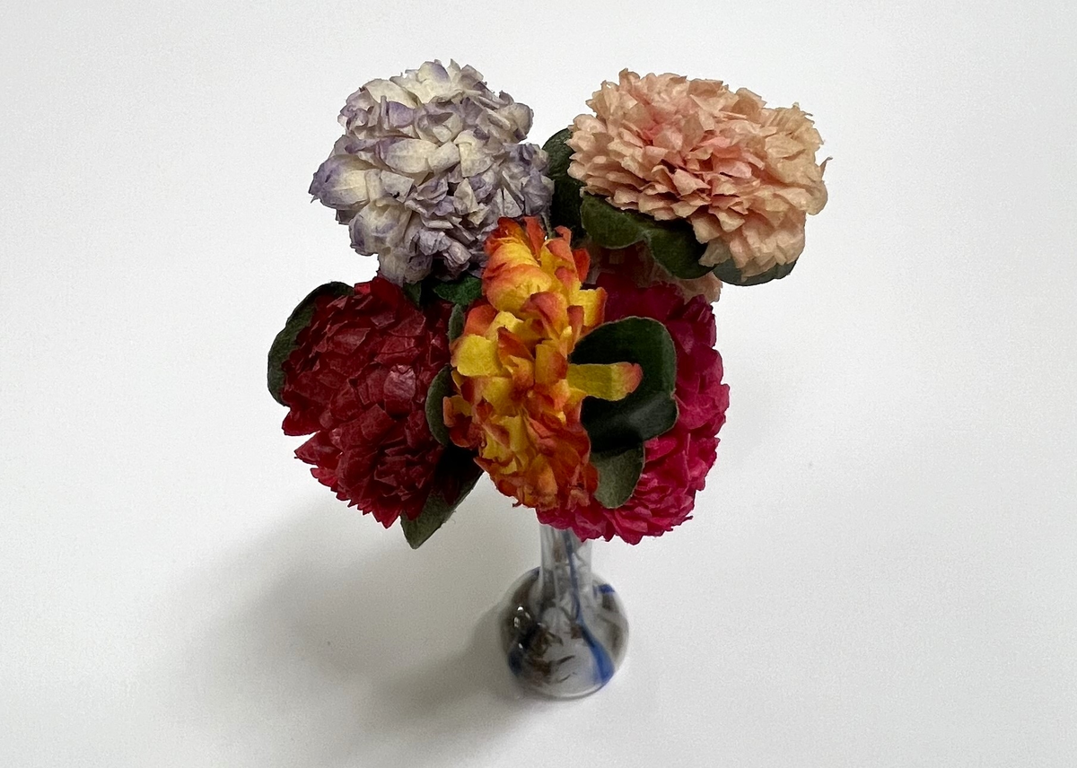 Glasvas med blå ränder. Pappersblommor i rosa, lila, gult och grönt.