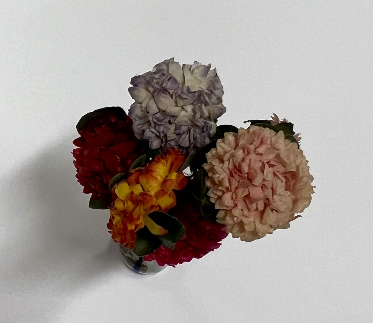 Glasvas med blå ränder. Pappersblommor i rosa, lila, gult och grönt.