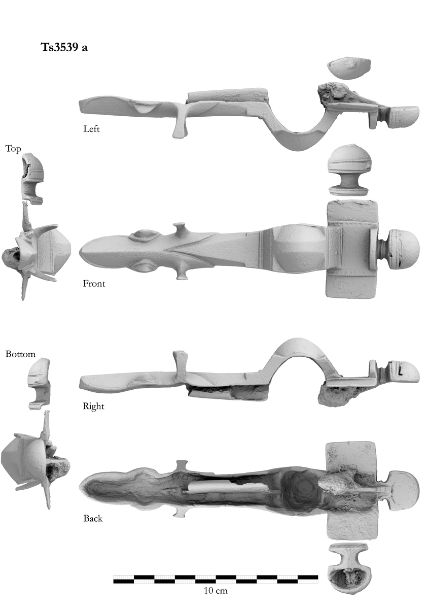 Korsformet spenne av bronse nærmest som Shetelig: Cruciform Brooches fig. 39, men i et senere utviklingstrinn. Dyrehodet nederst er skarpt rygget med en perlerand langs ryggen og konturen. Vingene ved mulen sitter forholdsvis høiere oppe og er skarpkantete, øinene består av tynne, vel 1,5 cm høie tapper, flate på utsiden. Ellers likner den meget cit. fig., men mangler sølvinnleggingen. Midtknoppen er støpt i ett med spennen. Den ses å være hul, men har påloddet en bronseplate. Den ene sideknopp foreligger løs. Nåleholderen forholdsvis kort. Rust etter nålen. Lengde 16,6 cm.