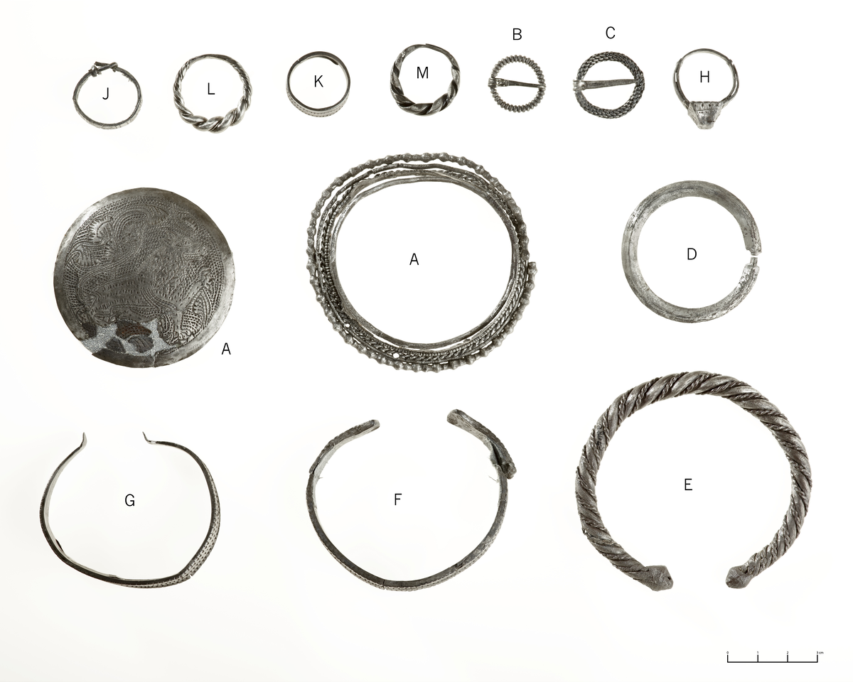 Ringspenne. Bortsett fra under tornfestet er hele ringen riflet helt rundt. Øvre del av tornen med ombøying er flat og inndelt i 3 "bånd", resten har firsidig tverrsnitt, spiss ytterst. Har f.eks. Serning, Lapska Offerplatsfynd, 1956, pl. 38 : 18. Indre diam. 1,4 cm, ytre 1,9, tornens l. 1,9 cm. Vekt etter prep. 3,6 gr. Tetthet 10,18 sølvgehalt.