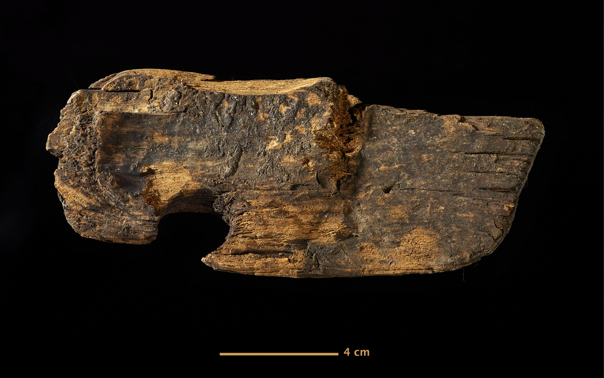 Gjenstand: Tre. Trestykke, skrått kuttet i den ene enden, tiln. buet i den andre. I den ene kanten er et hull, ant. kvisthull. 16.5x7 cm.