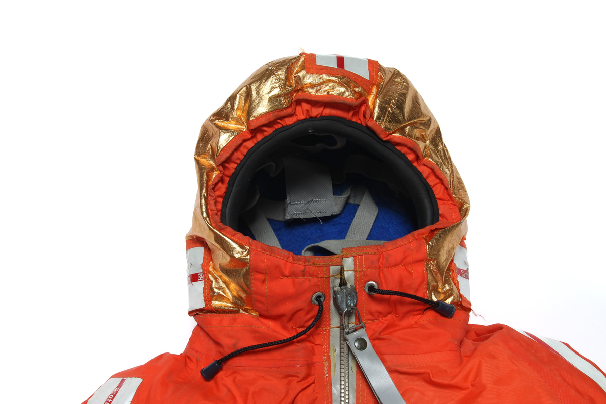 Redningsdrakt i størrelse medium med hette og sko. Hetten er belagt med metallfolie for isolasjon. Støvlene er limt og sveiset på og kan strammes til med snøring.
