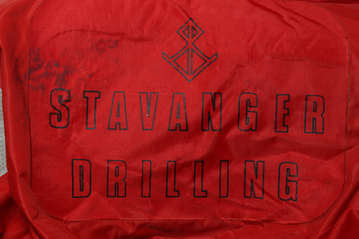 Redningsdrakt i størrelse medium med Stavanger Drilling sin logo på ryggen. 

Drakten er produsert av en flammebestandig neopren-nylonduk og utstyrt med fluorescerende ytterhette med påsydde reflekser. Den har løst innerfôr som er festet til drakten med borrelås. Faste flytemidler er plassert i lommer i fôret.
